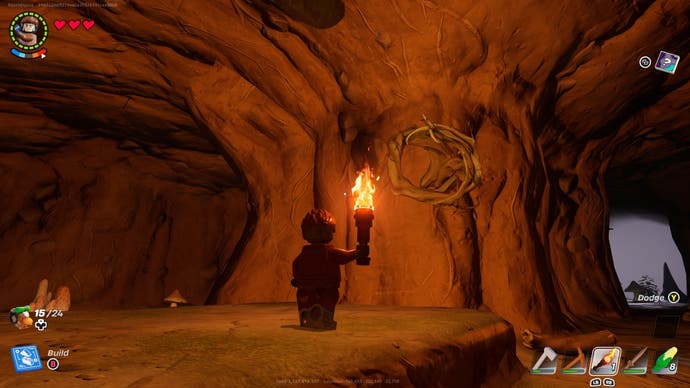 a lego character holding a lit torch looking up at knotwood growing from a cave wall